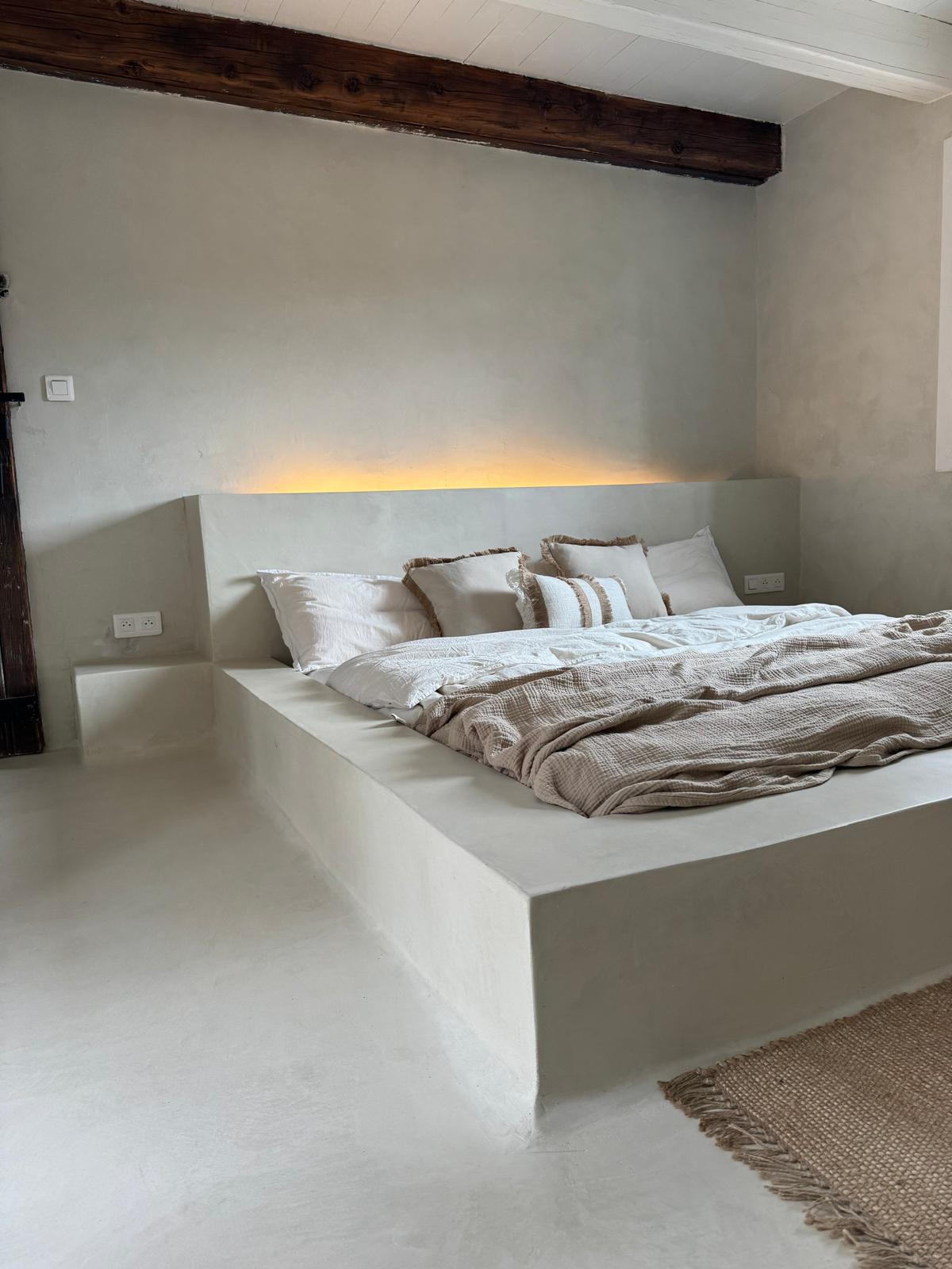Chambre épurée avec lit plateforme, lumière douce et sols raffinés dans l'esprit béton ciré.