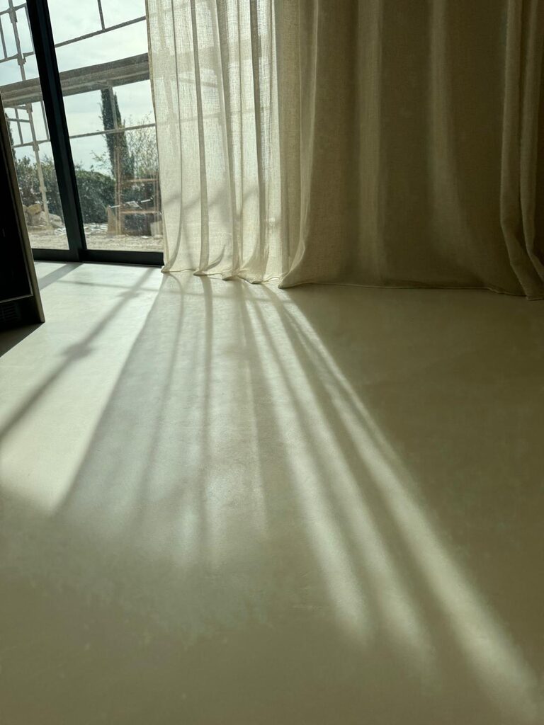 Élégante lumière naturelle sur sol lisse en béton ciré, au pied d'une grande fenêtre moderne.