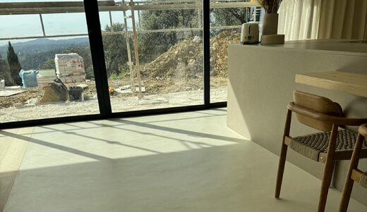 Espace épuré, sol clair, chaises bois, larges baies vitrées sur chantier et paysage.