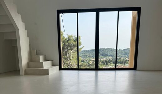 Espace minimaliste, sol blanc, escaliers, larges baies sur vue verdoyante et collines illuminées.