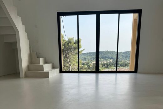Espace minimaliste, sol blanc, escaliers, larges baies sur vue verdoyante et collines illuminées.